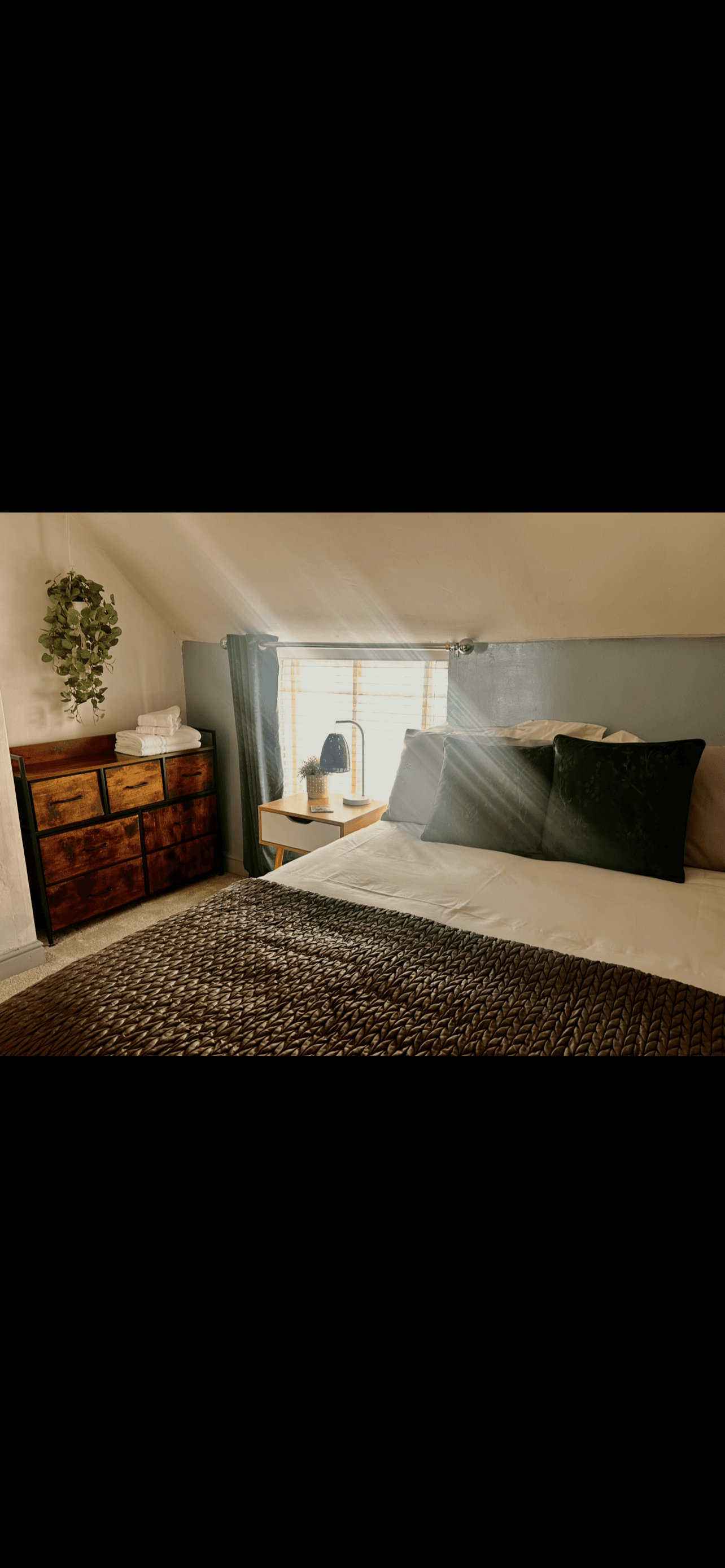 Sunlight streams into a cozy bedroom with green pillows and a brown textured coverlet.