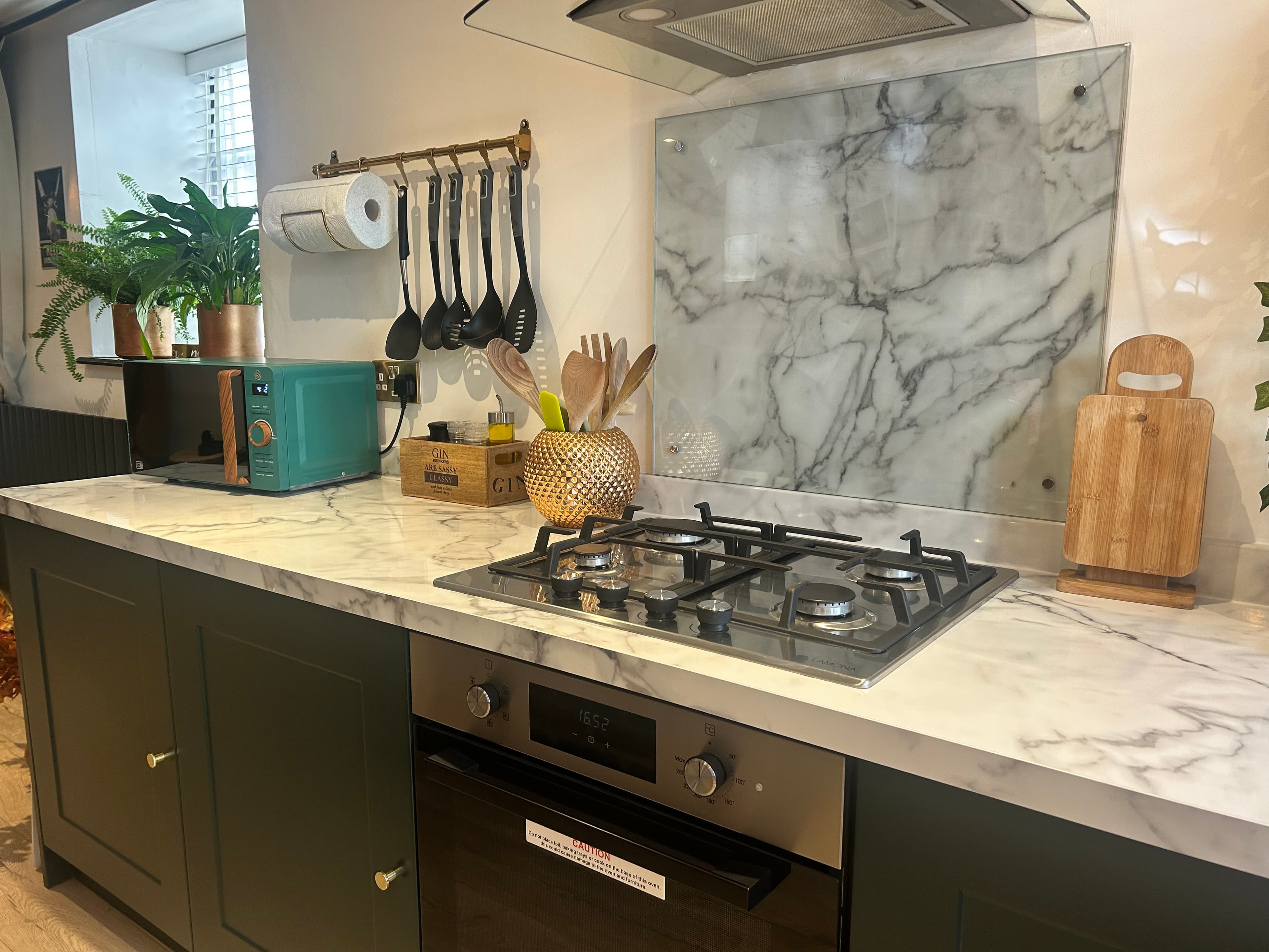 Modern kitchen featuring dark green cabinets, marble countertops, a gas stovetop, and teal microwave.