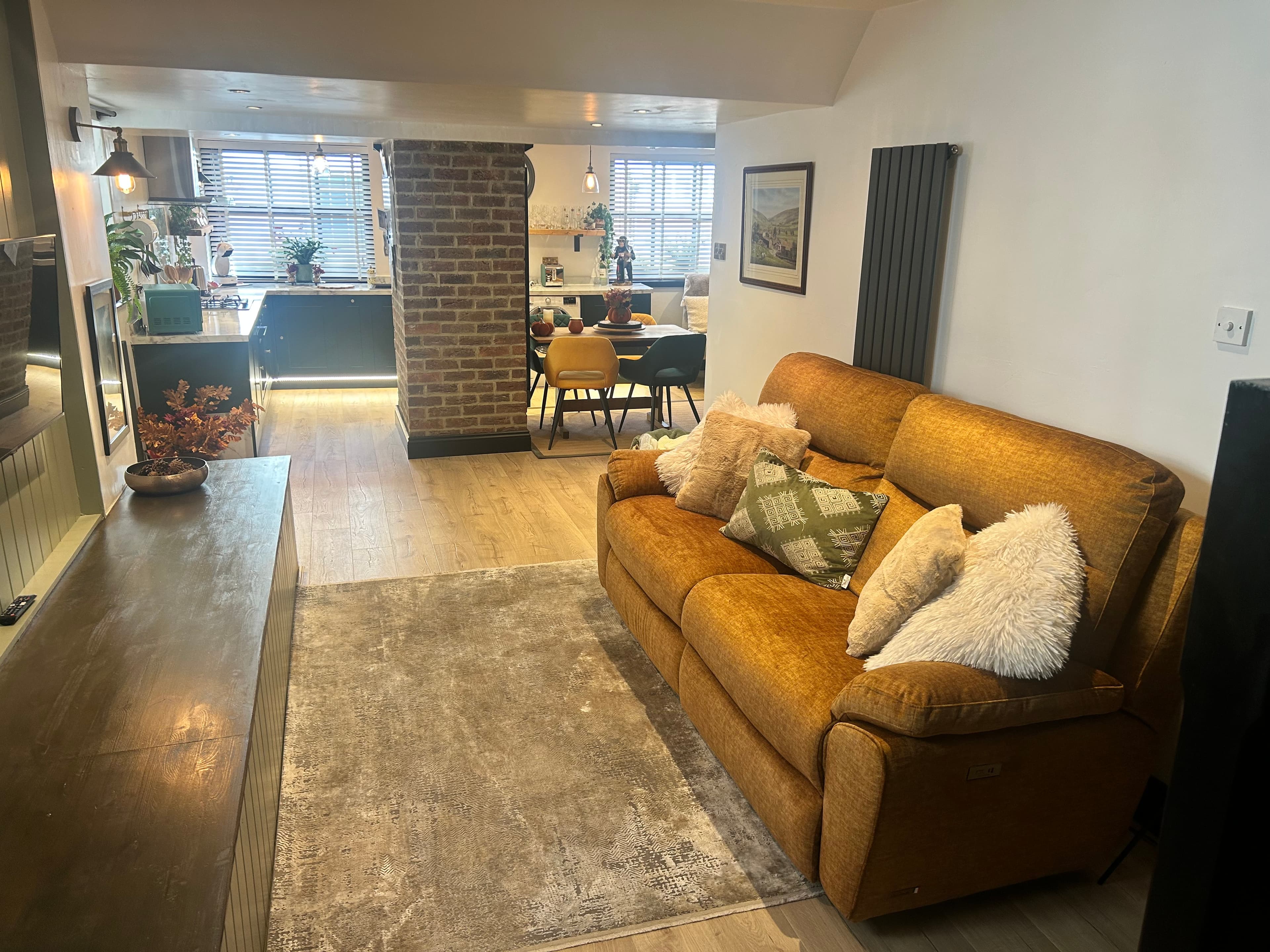 Cozy open-plan living area featuring a mustard yellow sofa, grey rug, and brick pillar.