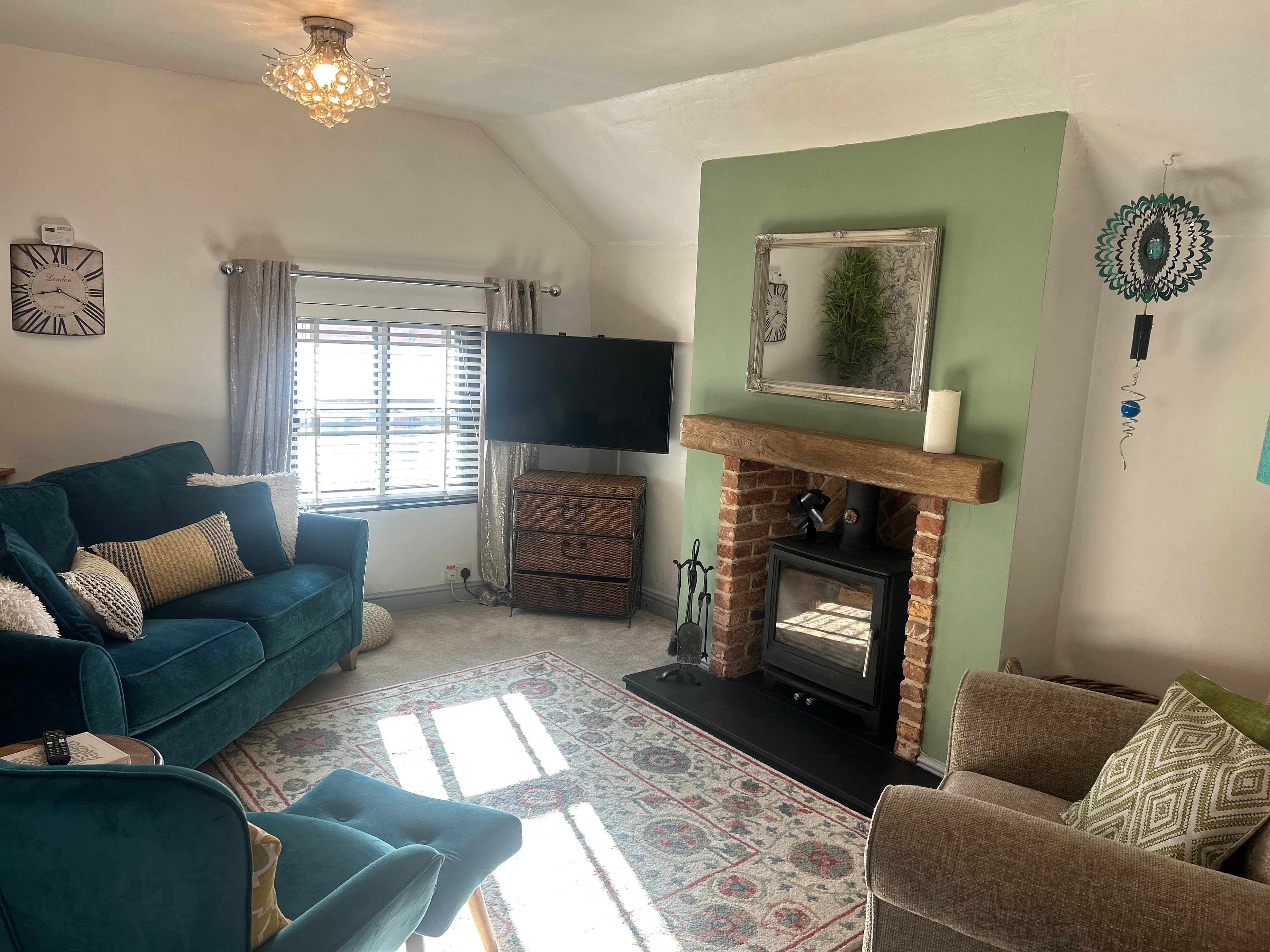 Cozy living room with teal velvet seating, wood-burning stove, and sage green accent wall.