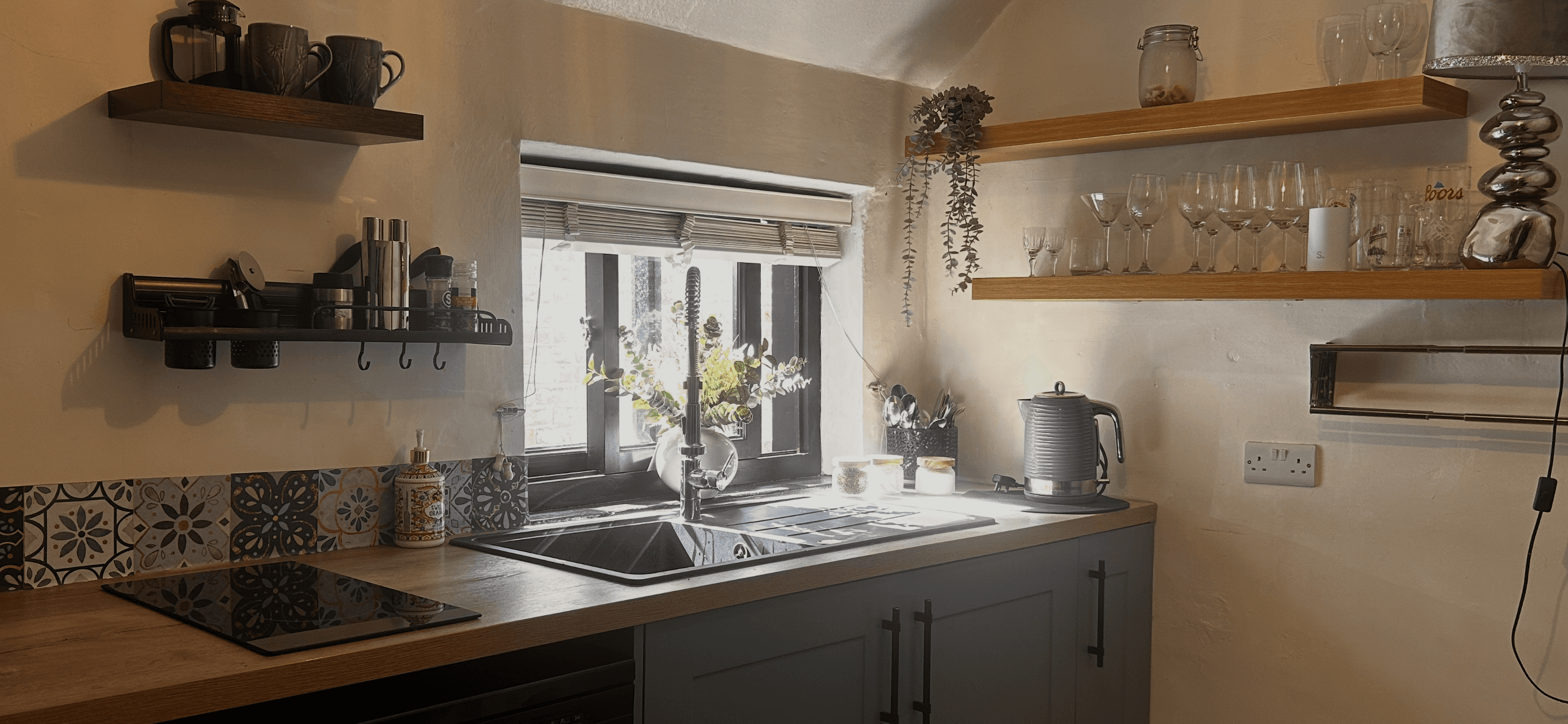 Rustic kitchen with a black sink, wooden countertops, and floating shelves under warm sunlight.